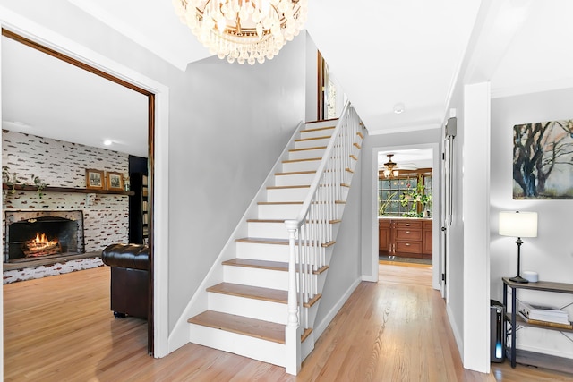 staircase featuring crown molding, a chandelier, baseboards, wood finished floors, and a lit fireplace