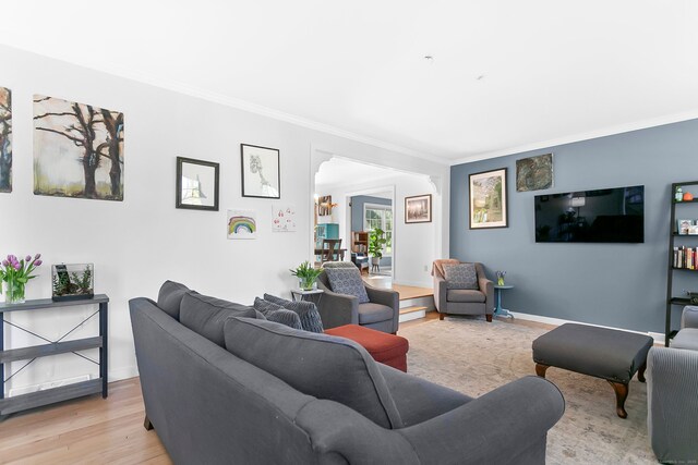 living room featuring crown molding, arched walkways, baseboards, and light wood-type flooring