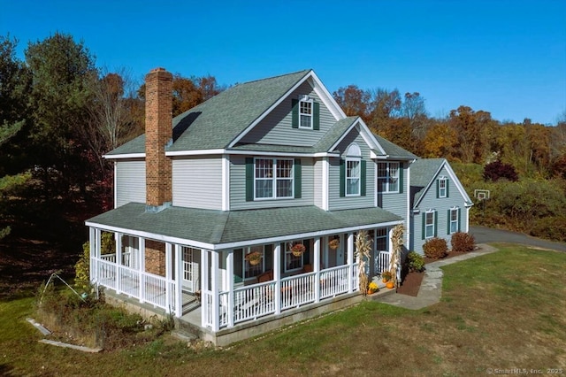 view of front facade featuring a front yard, a chimney, a porch, and a shingled roof