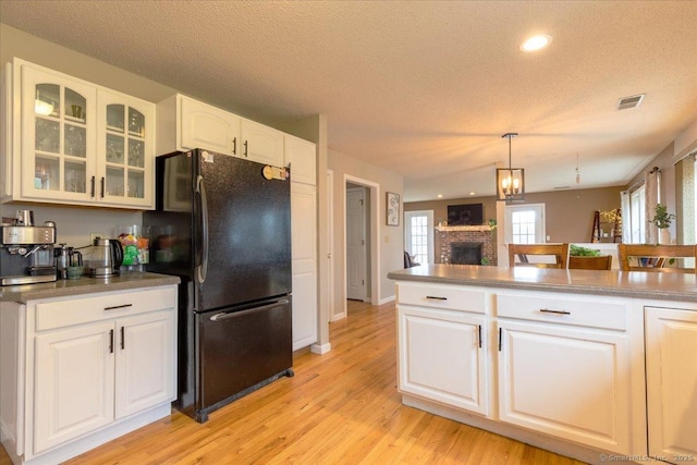 kitchen featuring a fireplace, glass insert cabinets, light wood-type flooring, visible vents, and freestanding refrigerator