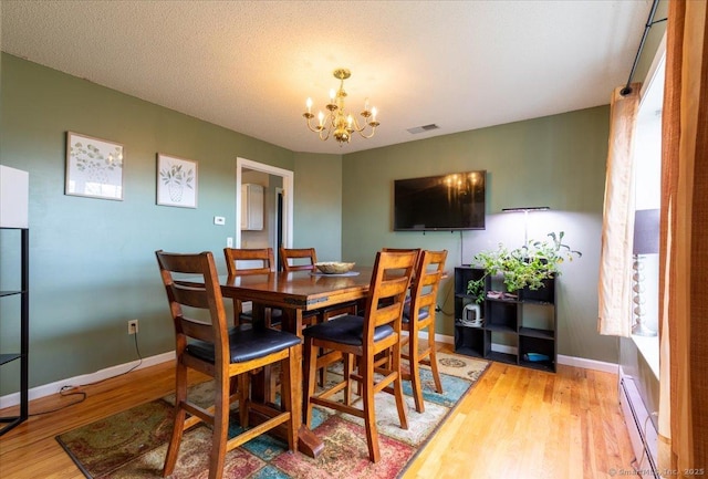 dining space with visible vents, baseboard heating, baseboards, an inviting chandelier, and light wood-type flooring