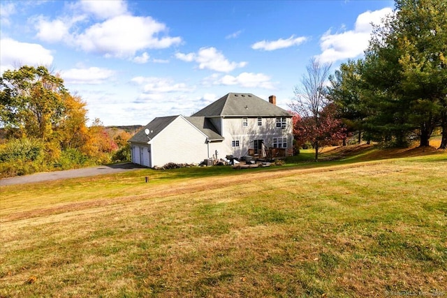 back of house featuring a chimney, aphalt driveway, a yard, and an attached garage