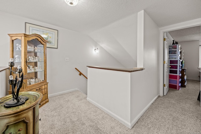 corridor featuring carpet flooring, a textured ceiling, an upstairs landing, and baseboards