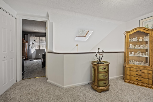 corridor featuring baseboards, carpet flooring, lofted ceiling with skylight, and a textured ceiling