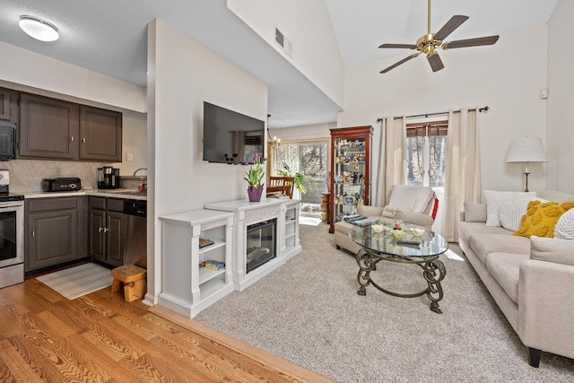 living room featuring ceiling fan, vaulted ceiling, light wood-style flooring, and visible vents
