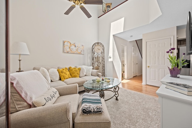 living room with baseboards, light wood finished floors, ceiling fan, and a towering ceiling