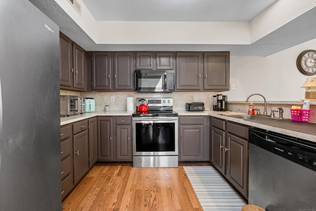kitchen featuring appliances with stainless steel finishes, tasteful backsplash, a sink, light countertops, and light wood-style flooring