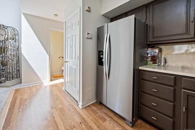 kitchen with stainless steel fridge, backsplash, dark brown cabinetry, and light wood-type flooring