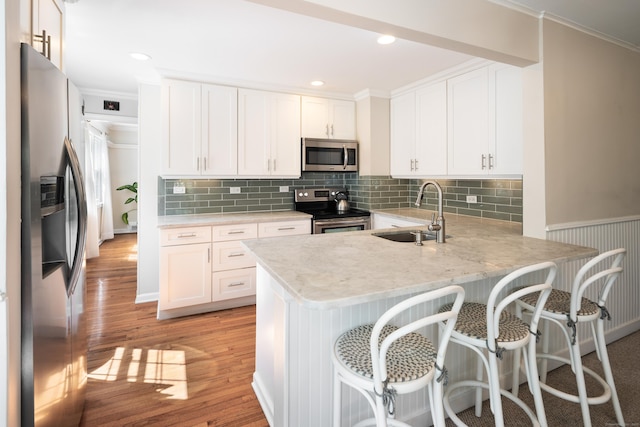 kitchen featuring a peninsula, light wood-style floors, white cabinets, a sink, and stainless steel appliances