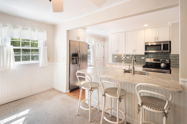 kitchen featuring wainscoting, a breakfast bar area, white cabinetry, a sink, and appliances with stainless steel finishes