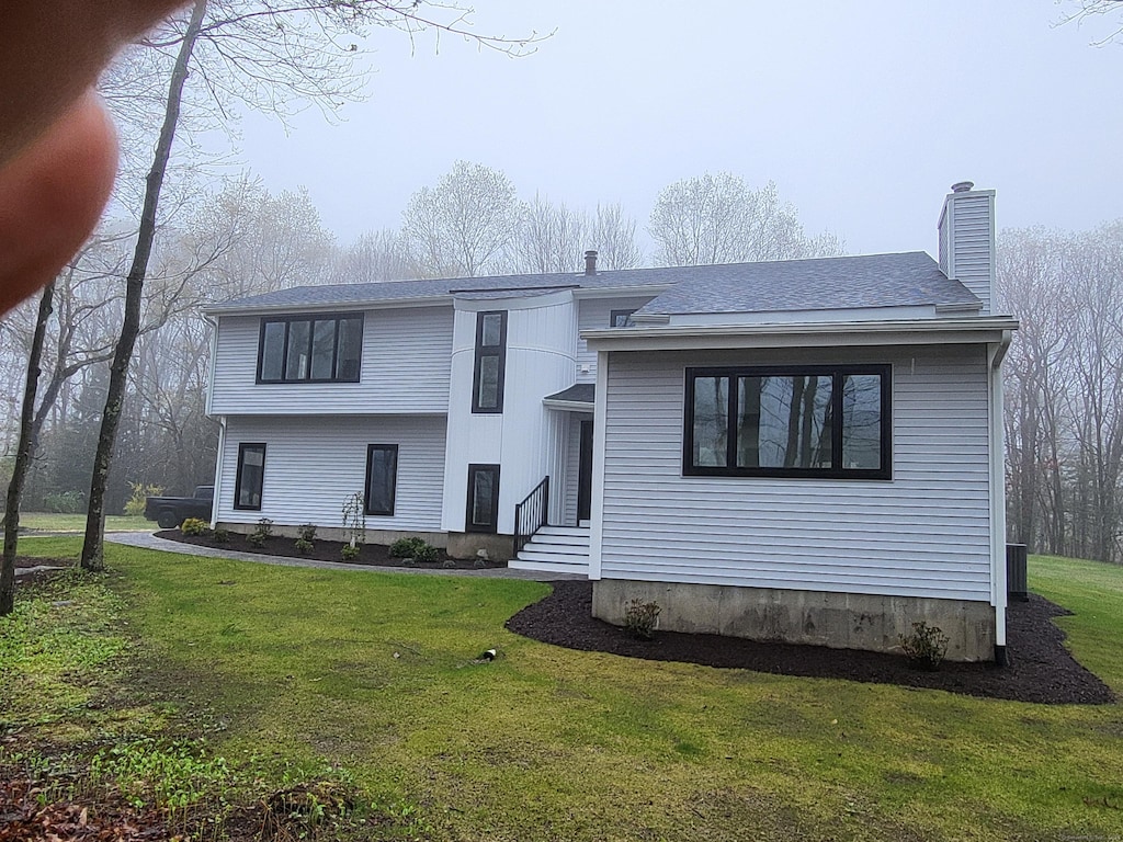 tri-level home with a chimney, a shingled roof, and a front lawn