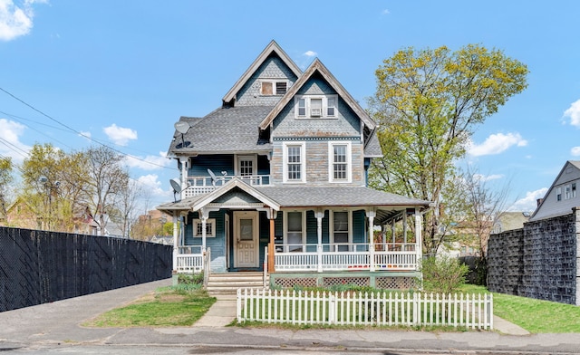 victorian-style house with covered porch, a shingled roof, and a fenced front yard