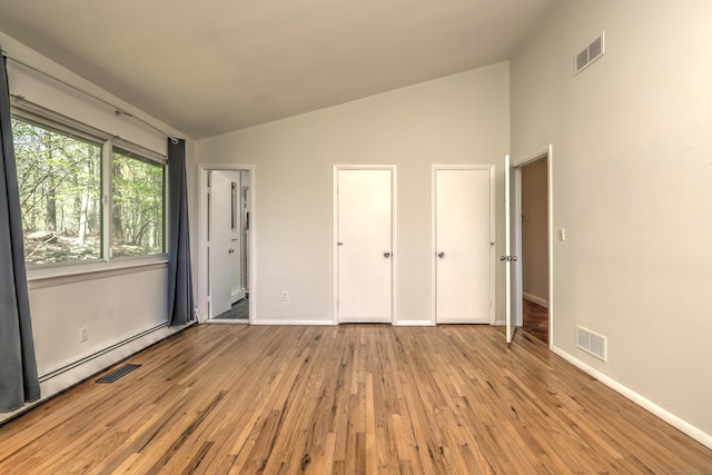 unfurnished bedroom with visible vents, light wood finished floors, and lofted ceiling