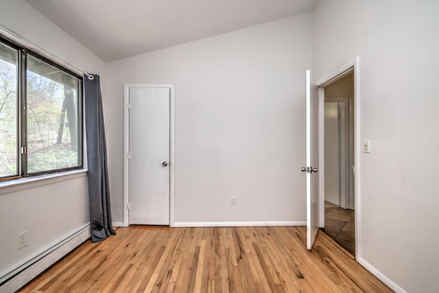 unfurnished bedroom featuring baseboards, light wood finished floors, lofted ceiling, and baseboard heating