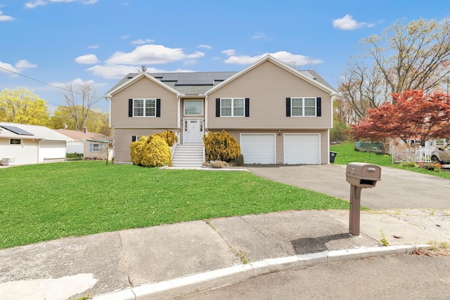 raised ranch with a front yard, an attached garage, aphalt driveway, and solar panels