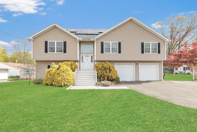 bi-level home featuring a garage, a front lawn, roof mounted solar panels, and driveway