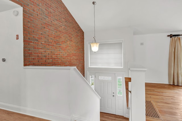 entrance foyer featuring baseboards, light wood-type flooring, brick wall, and high vaulted ceiling