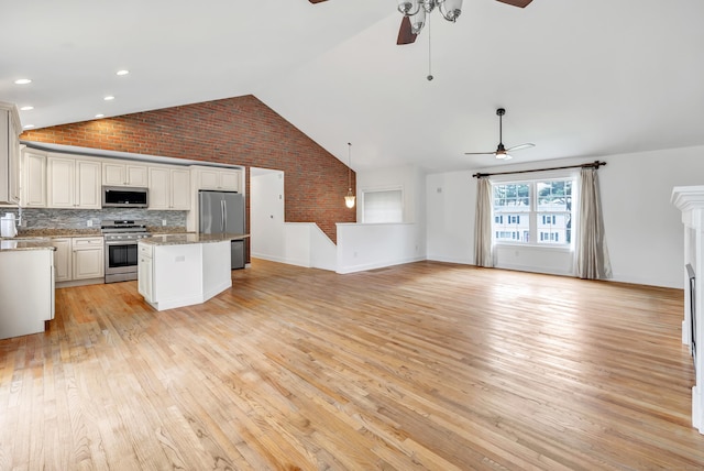 kitchen featuring appliances with stainless steel finishes, open floor plan, brick wall, vaulted ceiling, and a ceiling fan