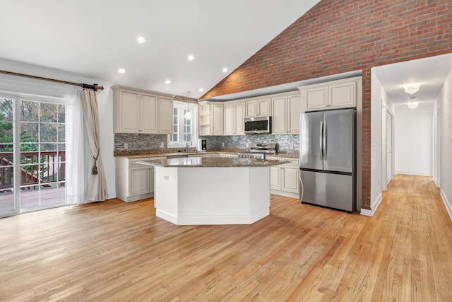 kitchen with appliances with stainless steel finishes, a healthy amount of sunlight, decorative backsplash, and high vaulted ceiling