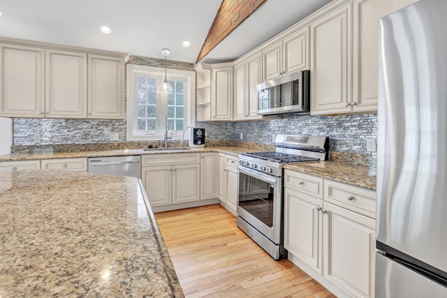 kitchen with light wood-style flooring, appliances with stainless steel finishes, vaulted ceiling, backsplash, and a sink