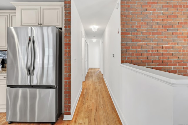 hall featuring baseboards, brick wall, and light wood-type flooring
