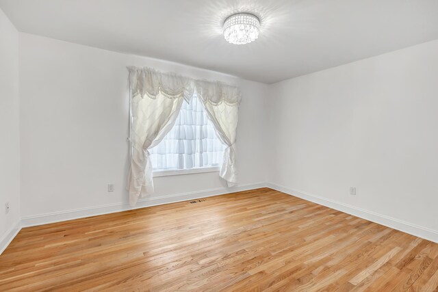 unfurnished room with baseboards, light wood-type flooring, and an inviting chandelier