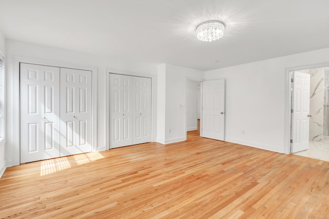 unfurnished bedroom with ensuite bath, two closets, a chandelier, baseboards, and light wood-type flooring