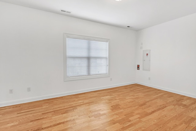 unfurnished room with visible vents, light wood-style flooring, electric panel, and baseboards