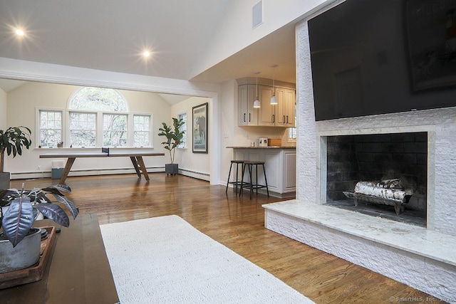 living room featuring baseboards, vaulted ceiling, a baseboard heating unit, and wood finished floors