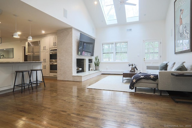 living area featuring visible vents, high vaulted ceiling, a large fireplace, dark wood finished floors, and a skylight