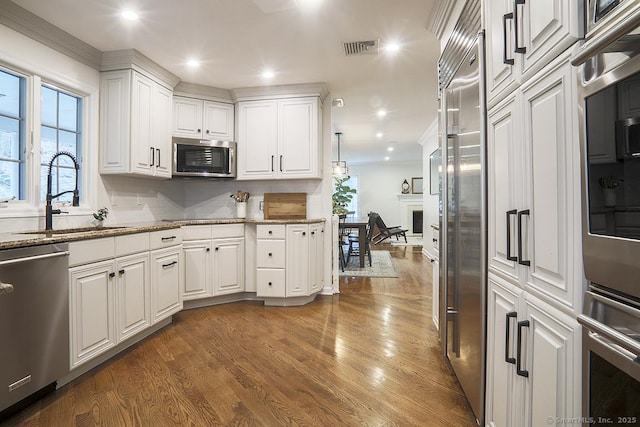 kitchen with visible vents, a sink, light stone counters, stainless steel appliances, and dark wood-type flooring