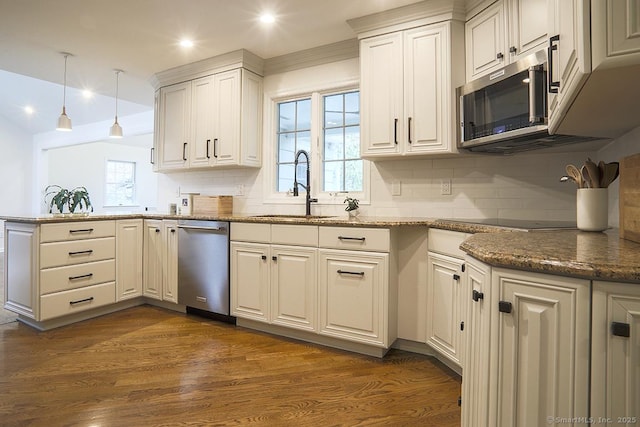 kitchen with appliances with stainless steel finishes, a sink, a peninsula, a healthy amount of sunlight, and tasteful backsplash