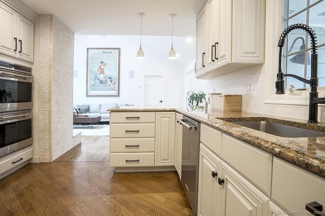 kitchen with a peninsula, light stone countertops, dark wood-type flooring, a sink, and appliances with stainless steel finishes
