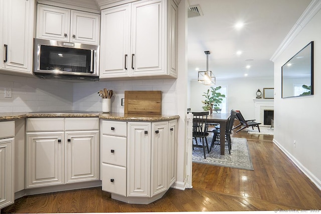 kitchen featuring dark wood-style flooring, white cabinetry, stainless steel microwave, baseboards, and backsplash