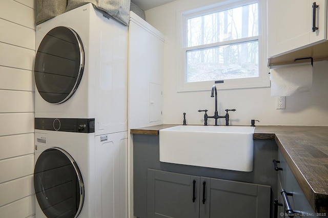 clothes washing area featuring cabinet space, stacked washer / drying machine, and a sink