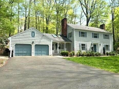 view of front of home with driveway, a chimney, a front lawn, and a garage