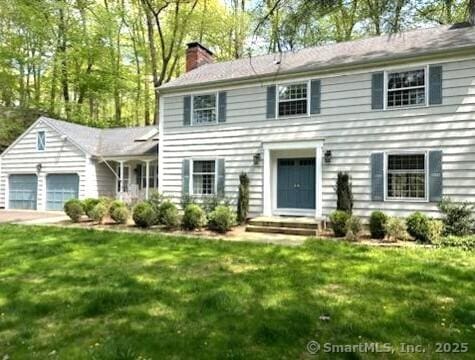 colonial inspired home featuring an attached garage, a front lawn, and a chimney