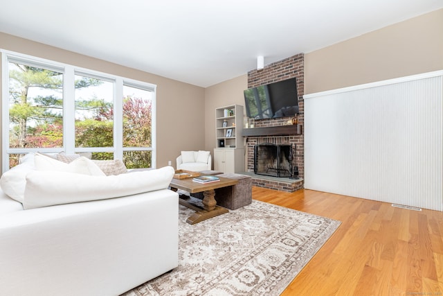 living room with a brick fireplace, visible vents, and wood finished floors