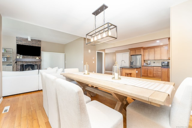dining space with a brick fireplace, light wood-style flooring, and visible vents