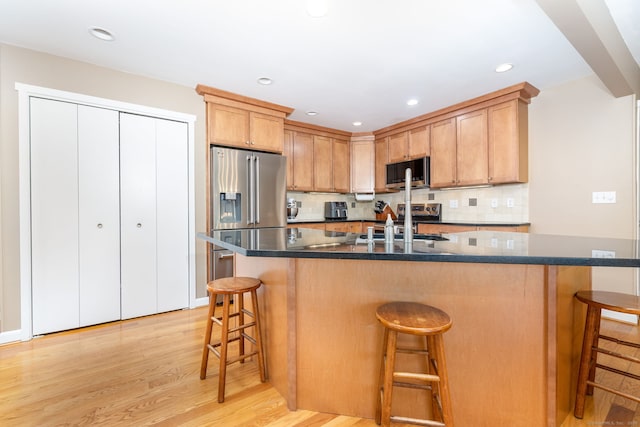 kitchen with appliances with stainless steel finishes, a breakfast bar, a sink, light wood finished floors, and backsplash