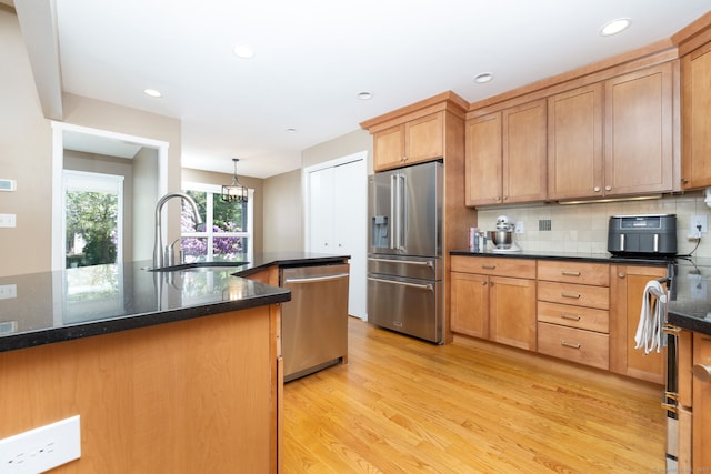 kitchen featuring appliances with stainless steel finishes, a sink, light wood-style flooring, dark stone countertops, and tasteful backsplash