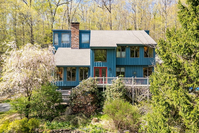 view of front of house with a shingled roof, a wooden deck, french doors, and a chimney