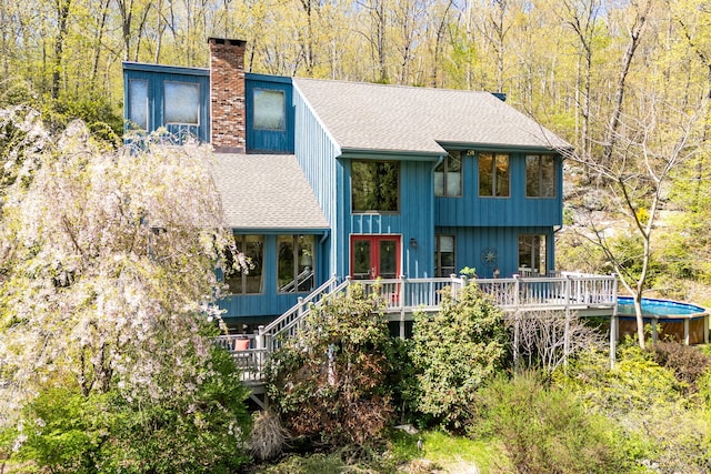 view of front of property featuring french doors, a deck, a chimney, and roof with shingles