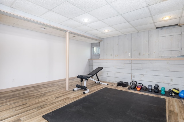 exercise room featuring a paneled ceiling, recessed lighting, baseboards, and wood finished floors