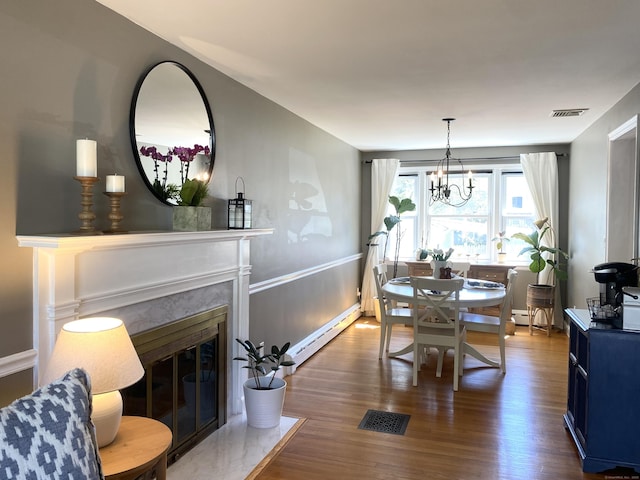 dining room featuring a baseboard heating unit, wood finished floors, visible vents, and a fireplace