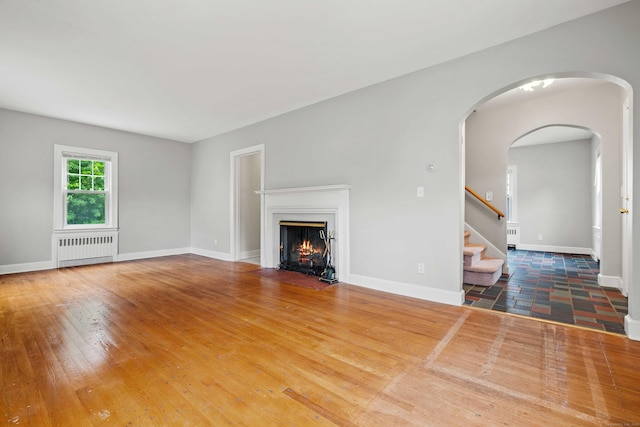 240 Barbara Rd, Middletown, CT 06457 - unfurnished living room with radiator heating unit, a fireplace with flush hearth, wood finished floors, stairway, and arched walkways