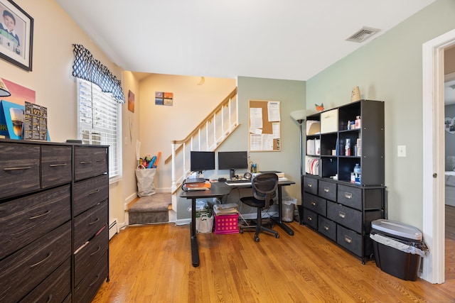 office featuring a baseboard heating unit, visible vents, light wood-style flooring, and baseboards