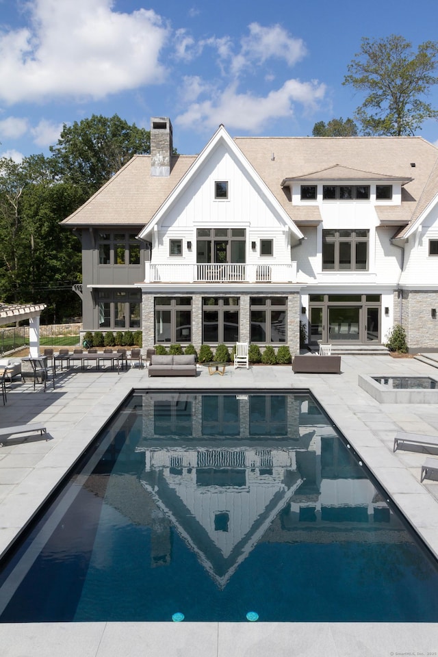 rear view of property featuring board and batten siding, a patio area, a balcony, and a chimney