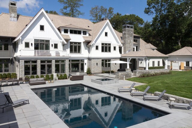 rear view of property with board and batten siding, an outdoor pool, a chimney, a patio area, and a balcony