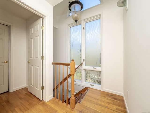 hallway featuring baseboards, wood finished floors, and an upstairs landing